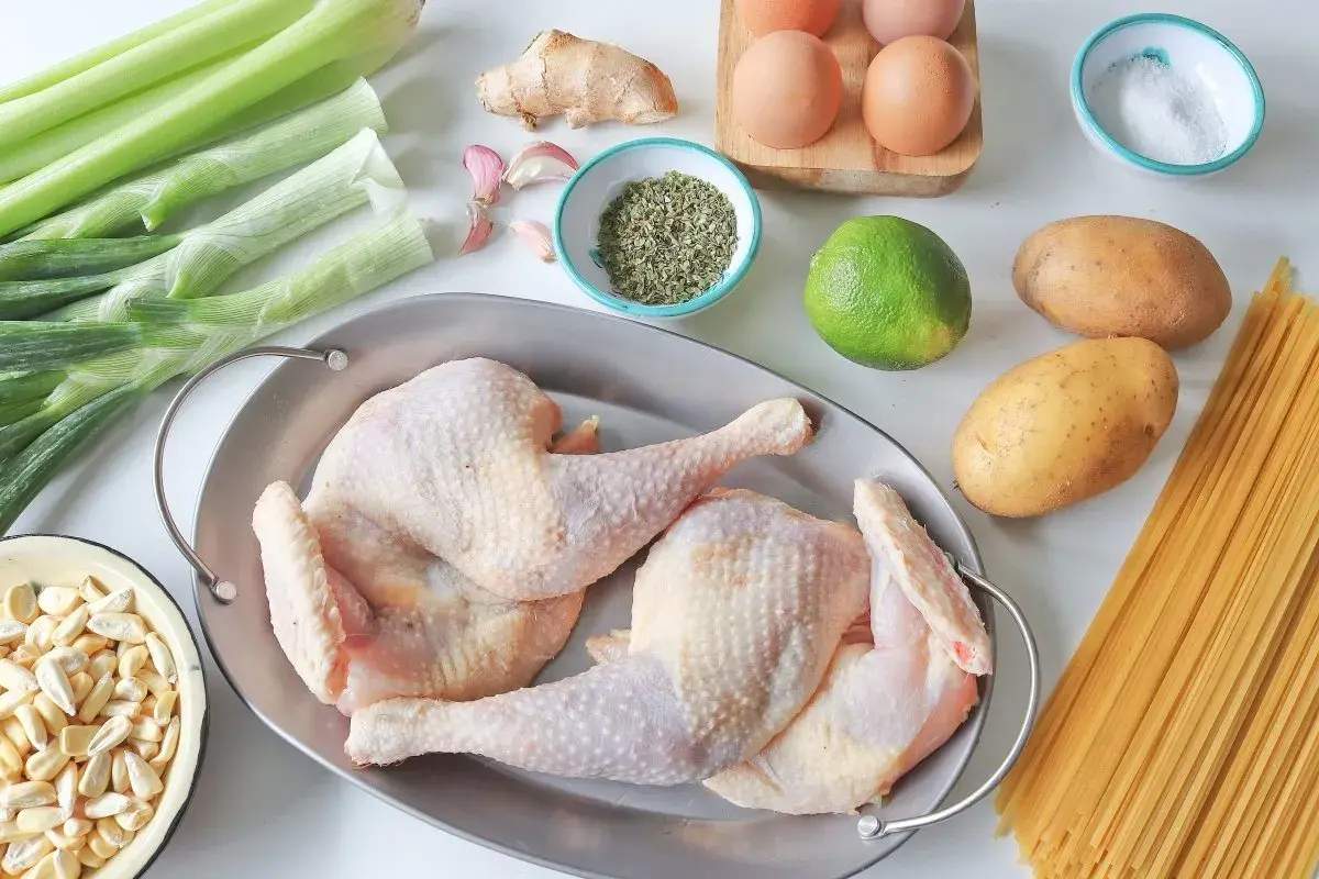 Ingredientes para un reconfortante caldo de gallina: pollo crudo, apio, cebolla, ajo, jengibre, papas, lima, especias, sal y pasta.