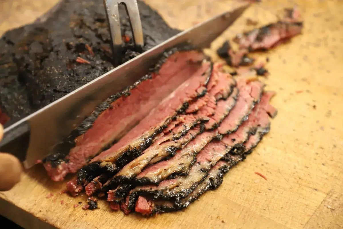 Un cuchillo corta un trozo de pastrami ahumado y jugoso, revelando su interior rosado.