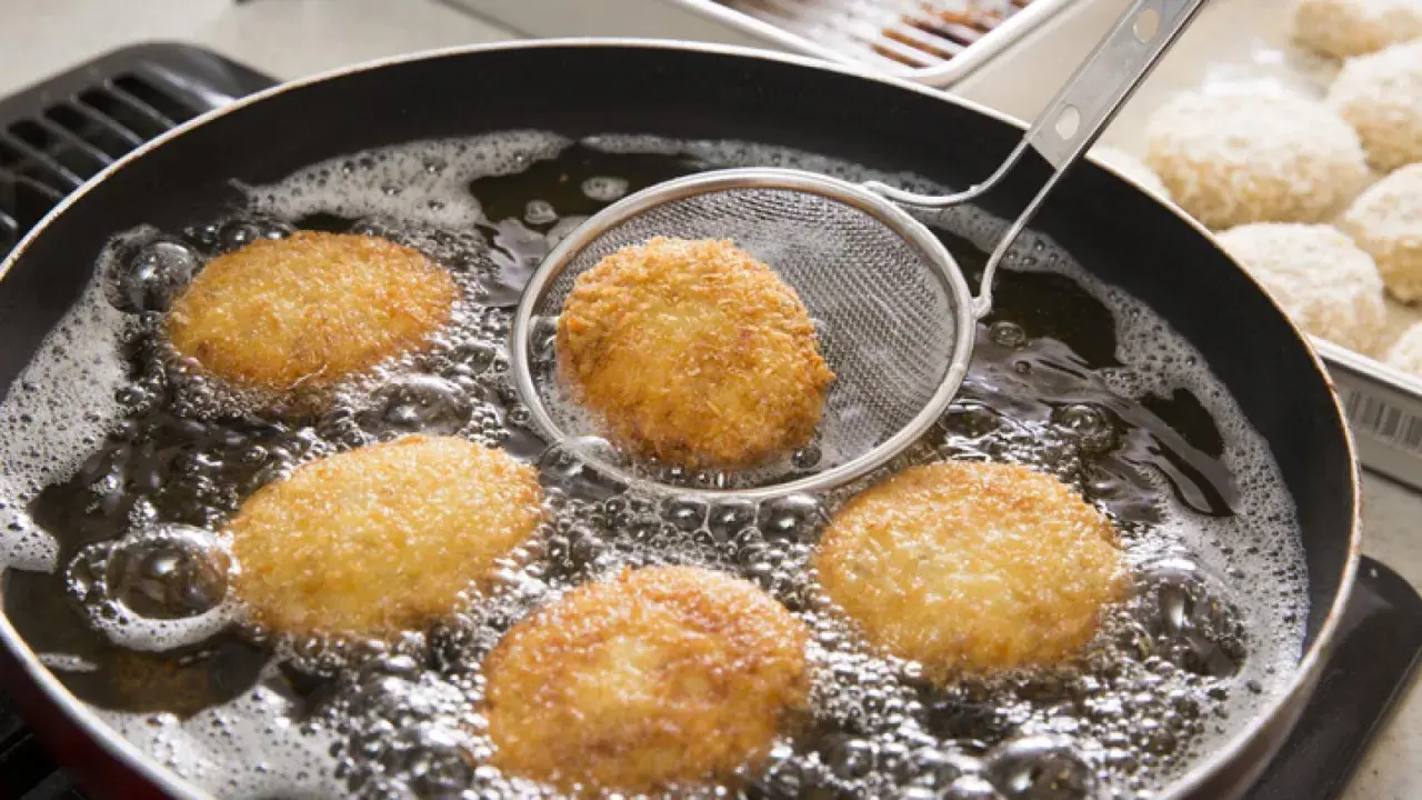 Croquetas doradas friéndose en aceite burbujeante, listas para ser disfrutadas. La bechamel para croquetas se transforma en esta delicia crujiente.