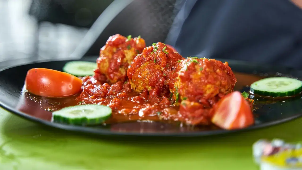 Albondigas con tomate, jugosas y cubiertas de salsa roja, acompañadas de rodajas de pepino y tomate fresco.