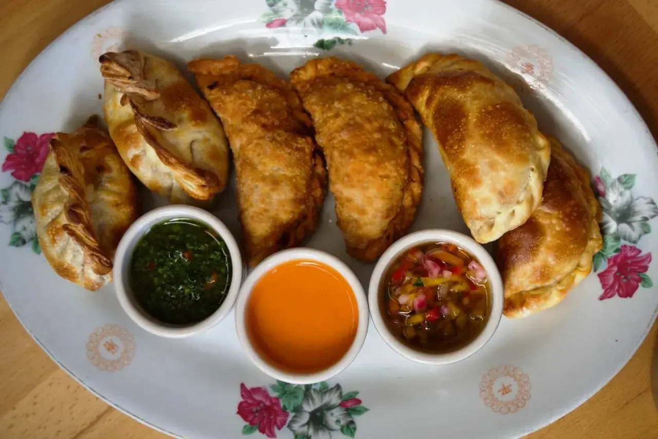 Empanadas de carne doradas y crujientes, servidas con tres salsas: chimichurri, picante y criolla.