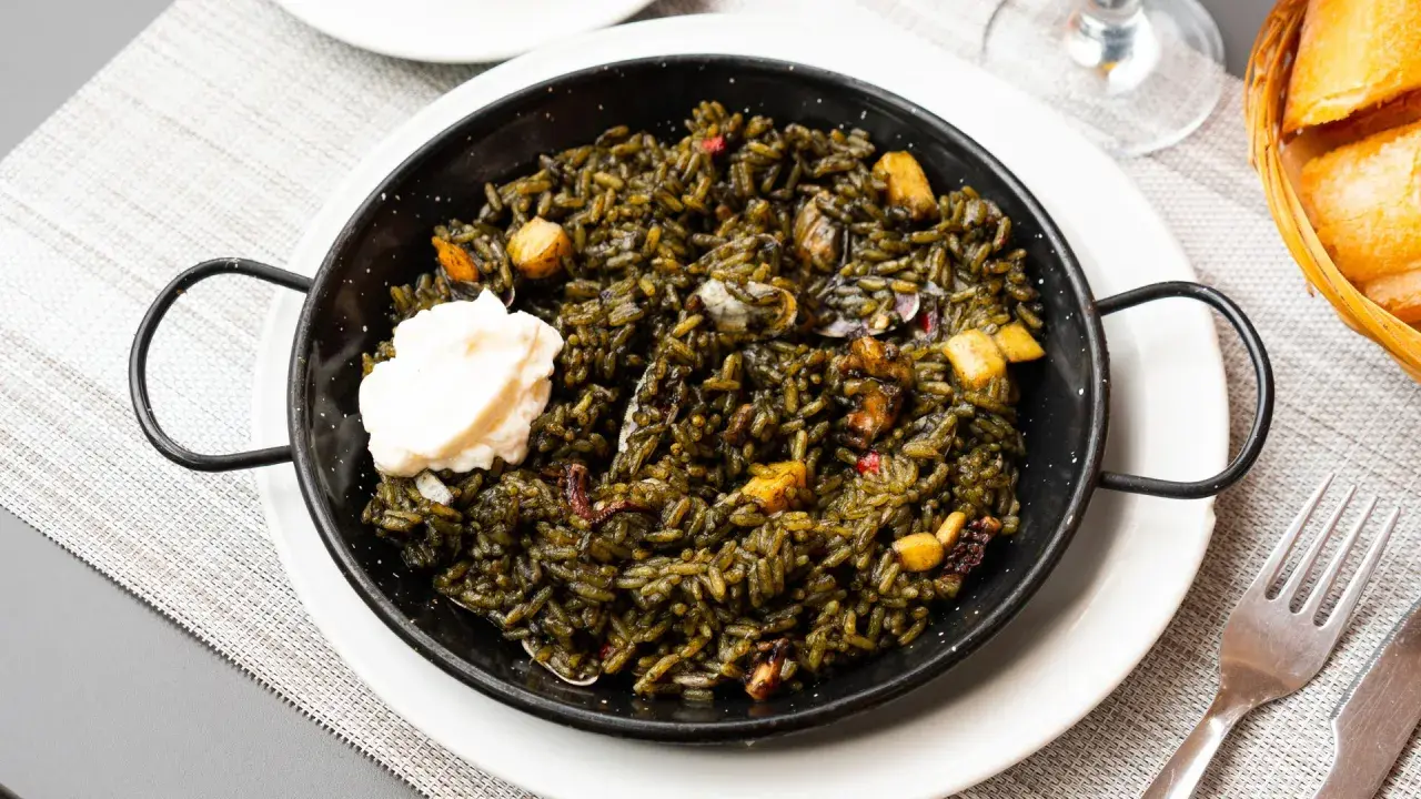 Arroz negro con sepia, un plato de mariscos oscuro y sabroso, servido en una paellera con una cucharada de alioli.