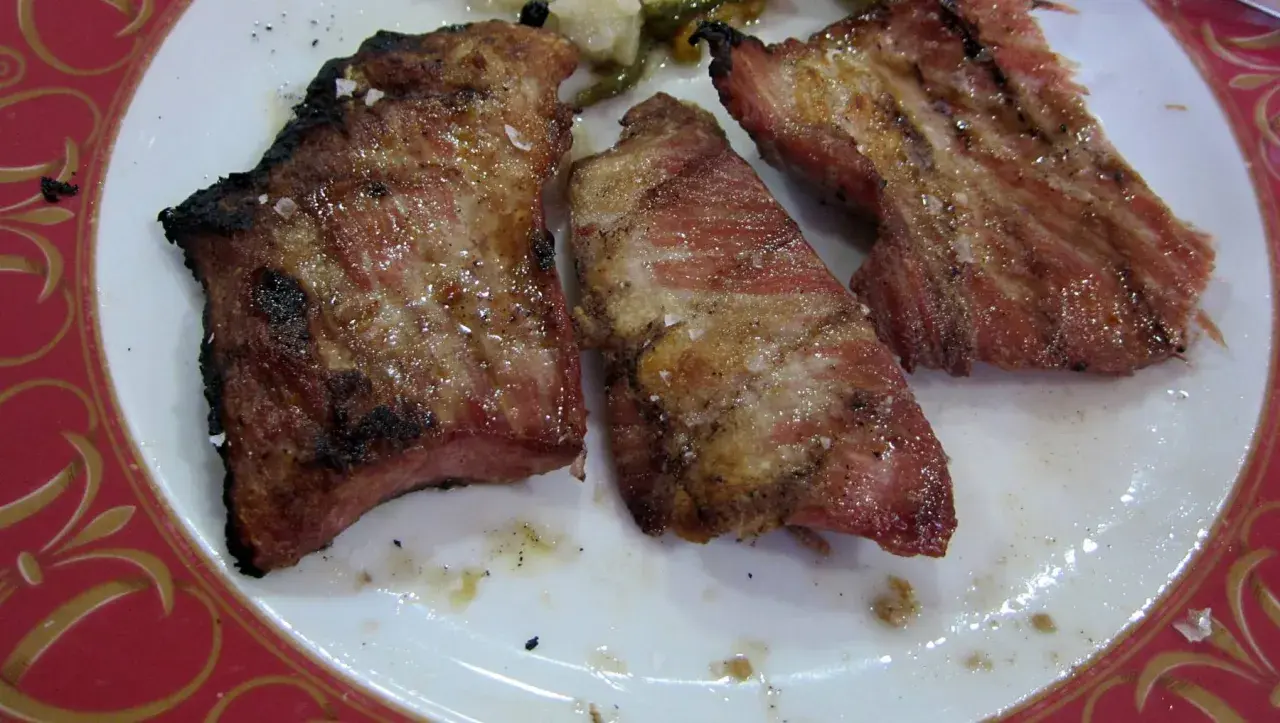 El secreto de cerdo a la parrilla, jugoso y con sal gruesa, servido en un plato blanco con borde rojo.