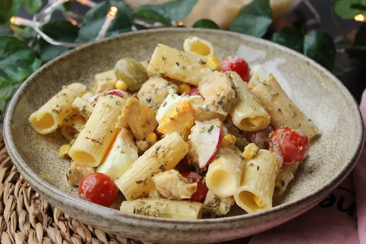 Deliciosa ensalada de pasta con pollo, huevo duro, tomates cherry, aceitunas y maíz, aderezada con hierbas.