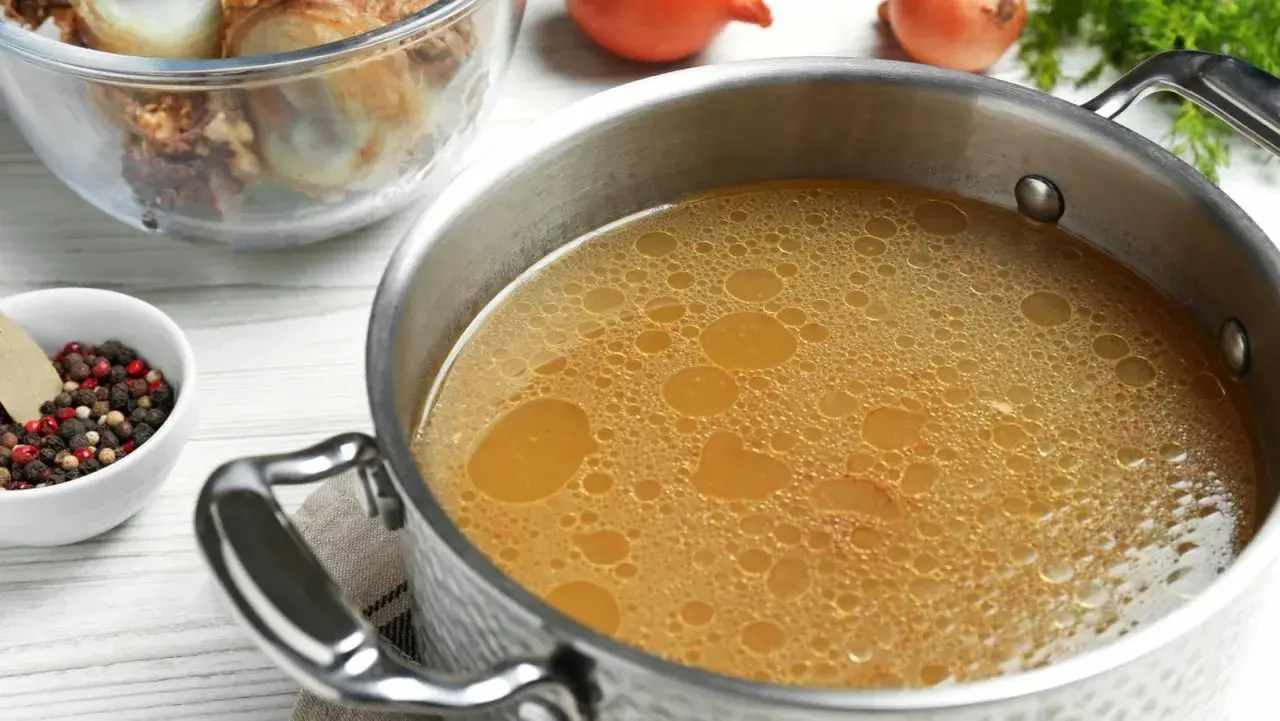 Olla con caldo de huesos burbujeante, junto a un bol con granos de pimienta y laurel, y otro con huesos.