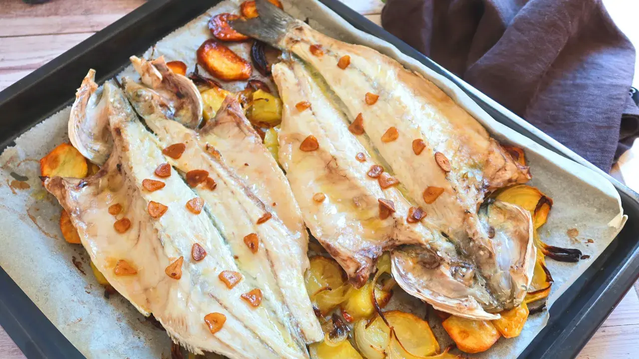 Lubina a la donostiarra recién horneada, con patatas y ajos dorados. Un plato delicioso y fácil de preparar.
