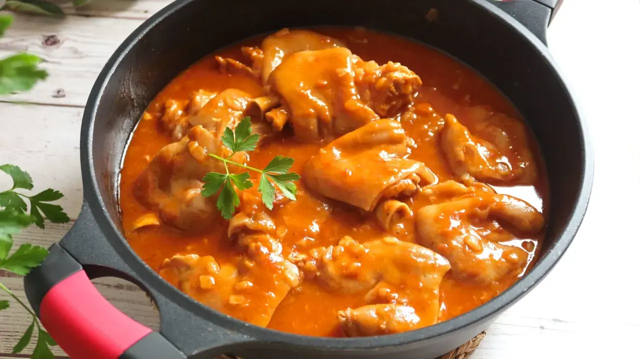 Manitas de cerdo en salsa roja, un plato tradicional español, servido en una sartén negra con perejil fresco.