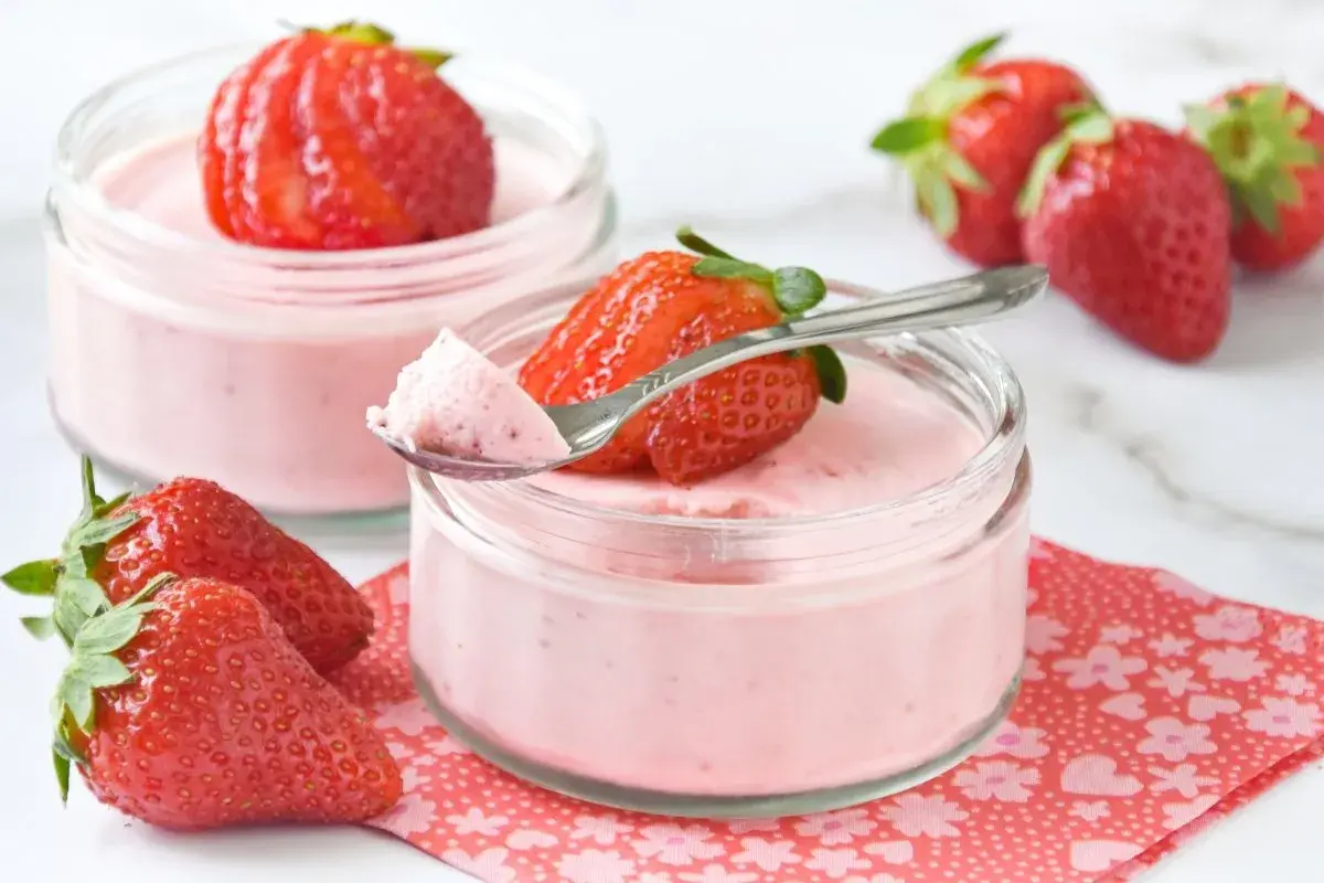 Delicioso mousse de fresa en vasitos, decorado con fresas frescas y una cucharita lista para probar.