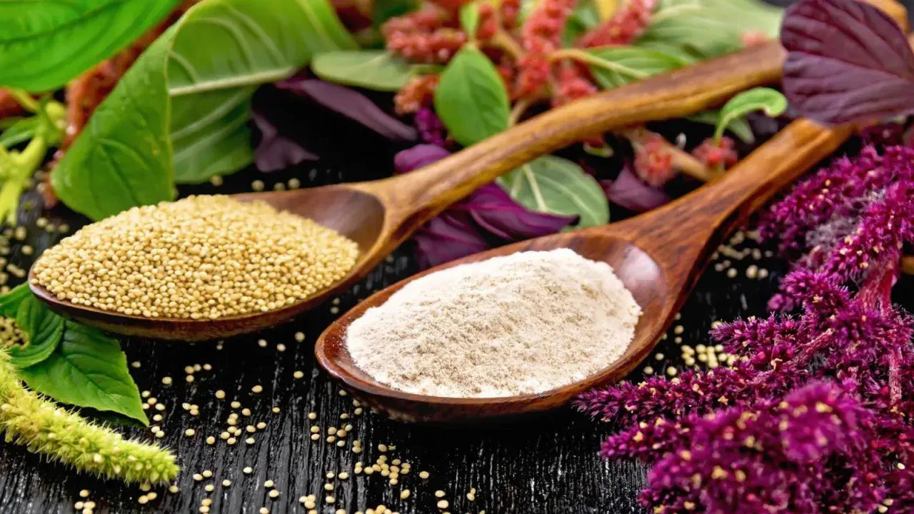 Cucharas de madera con semillas y harina de amaranto que es un grano ancestral, rodeadas de sus flores y hojas.