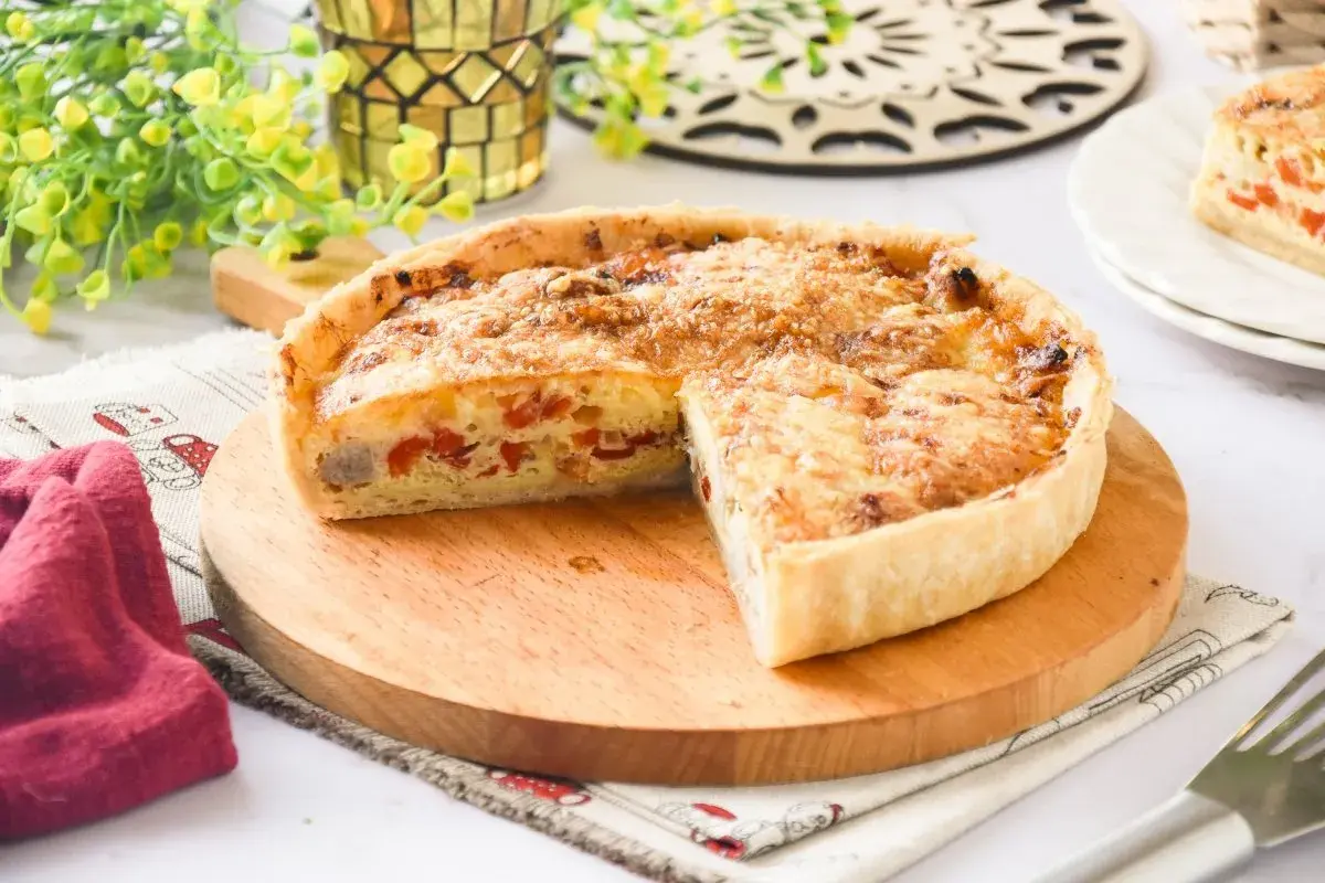 Un delicioso quiche de pollo, con trozos de pimiento rojo y queso gratinado, servido en una tabla de madera.
