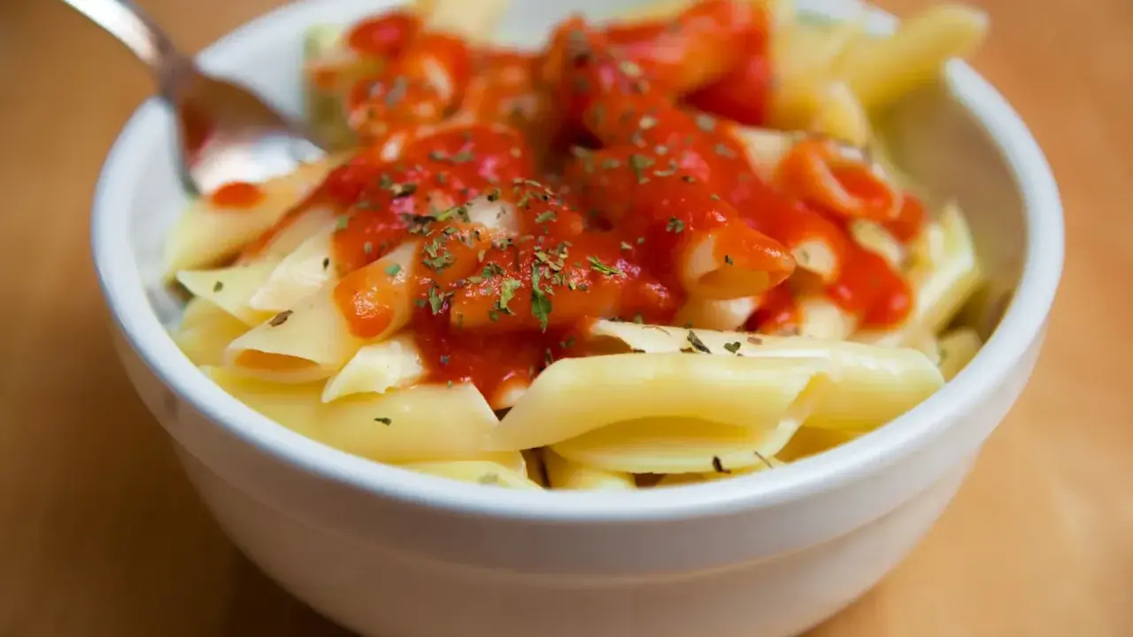 Un tazón de macarrones con tomate y hierbas, listo para disfrutar.