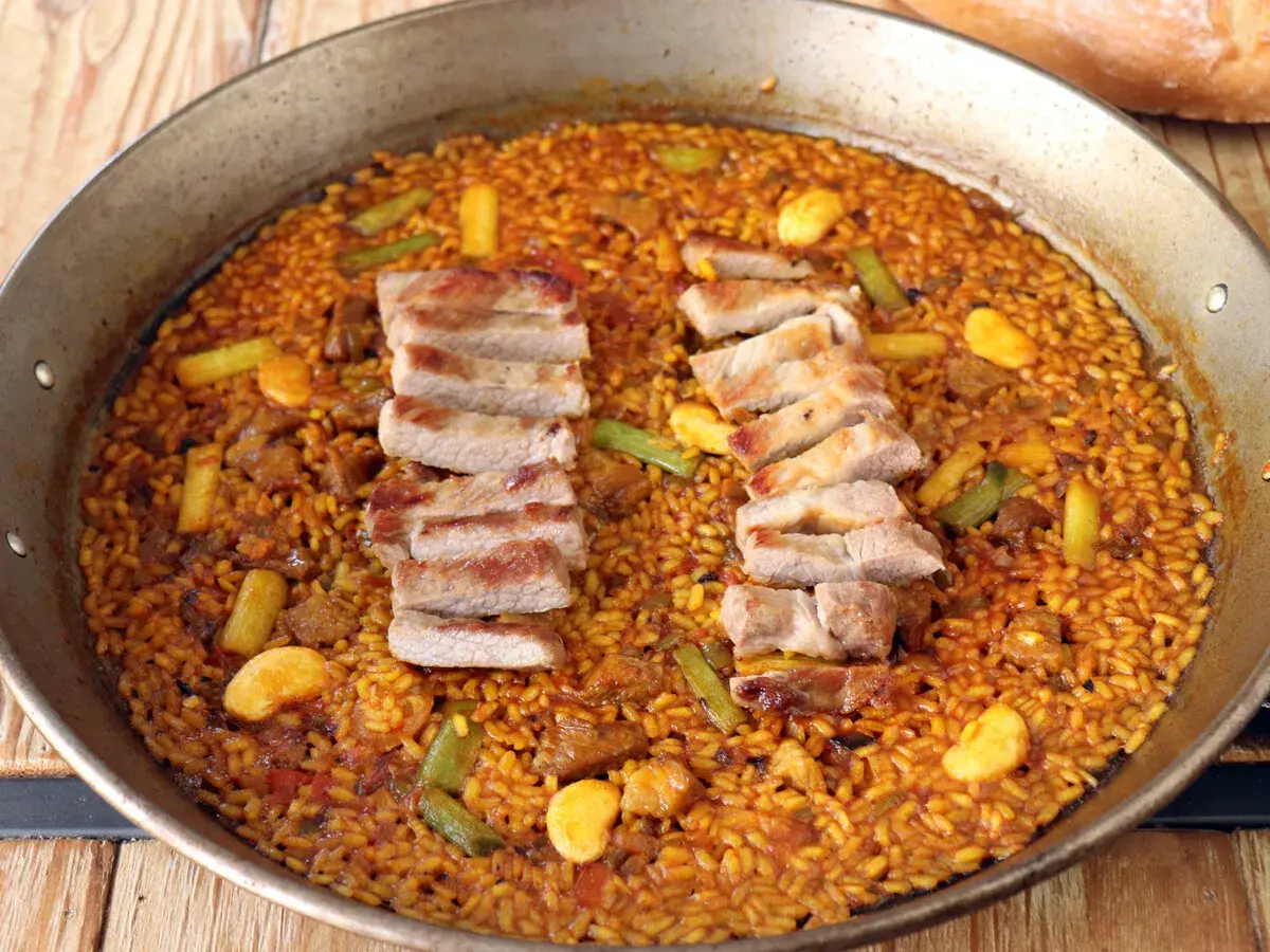Paella de secreto con trozos de cerdo a la parrilla, judías verdes y trozos de naranja.