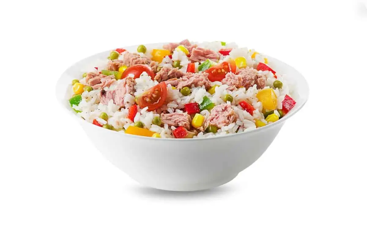 Un tazón blanco lleno de arroz con atún, guisantes, maíz, pimientos y tomates. Una comida fresca y colorida.