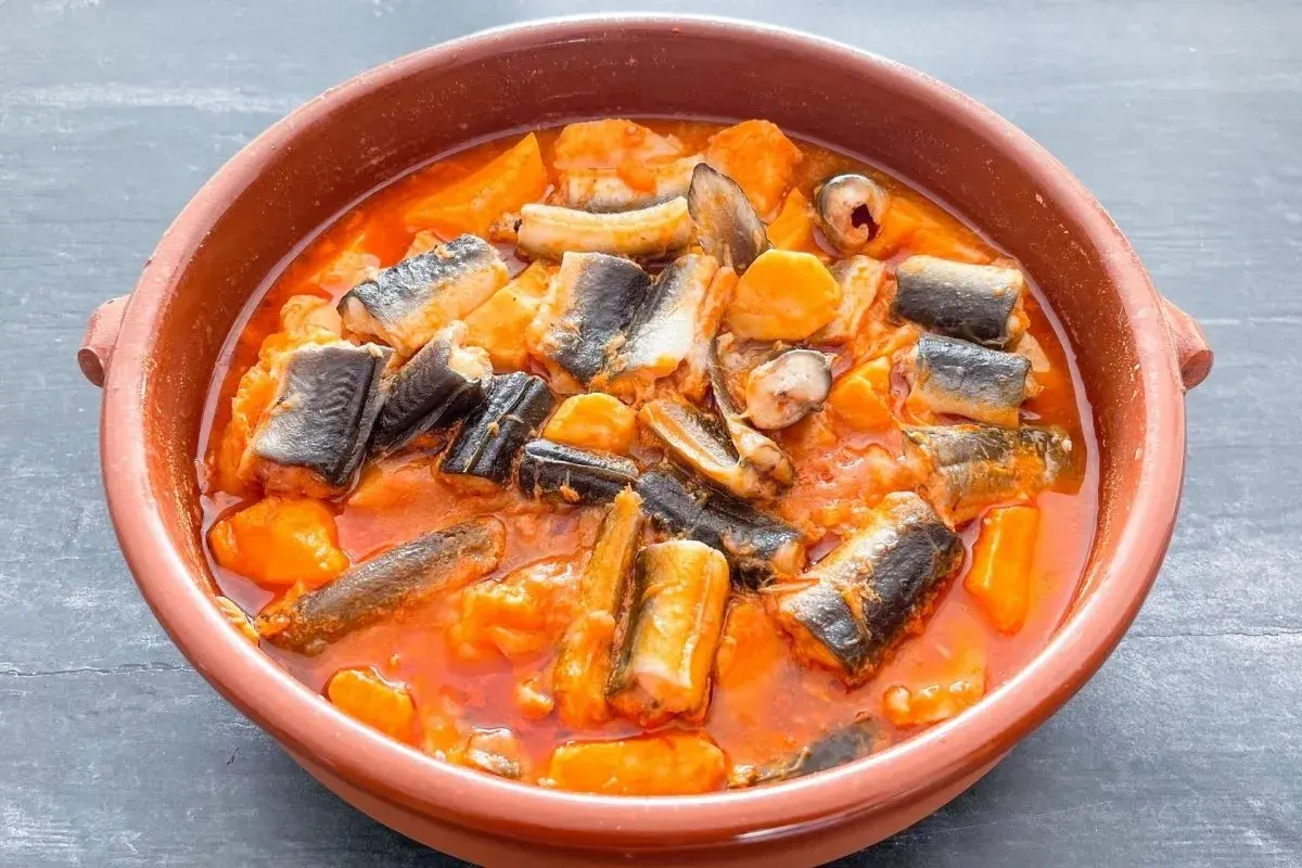 Un cuenco de barro con un sabroso all i pebre, un guiso tradicional de anguilas y patatas en salsa roja.