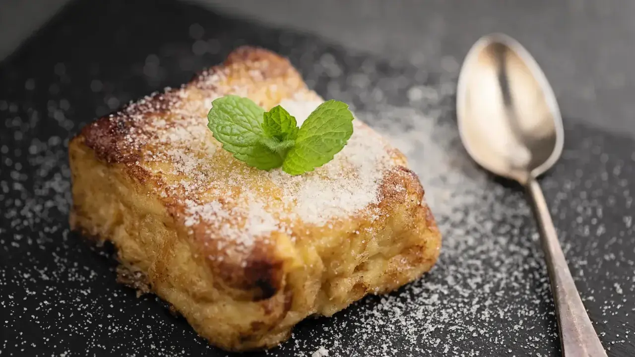 Torrijas con pan brioche, espolvoreadas con azúcar y decoradas con menta. Una cuchara plateada acompaña este delicioso postre.