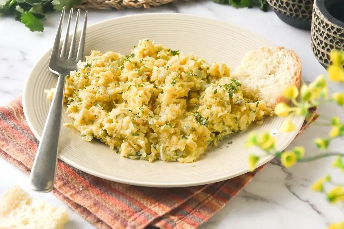 Un plato de bacalao a bras, desmenuzado y mezclado con patatas y perejil, servido con una rebanada de pan.