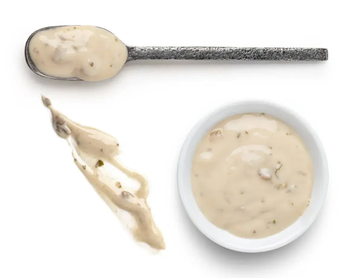 Cuchara con salsa de champiñones cremosa, un chorrito de la misma salsa y un cuenco blanco lleno de esta deliciosa salsa.