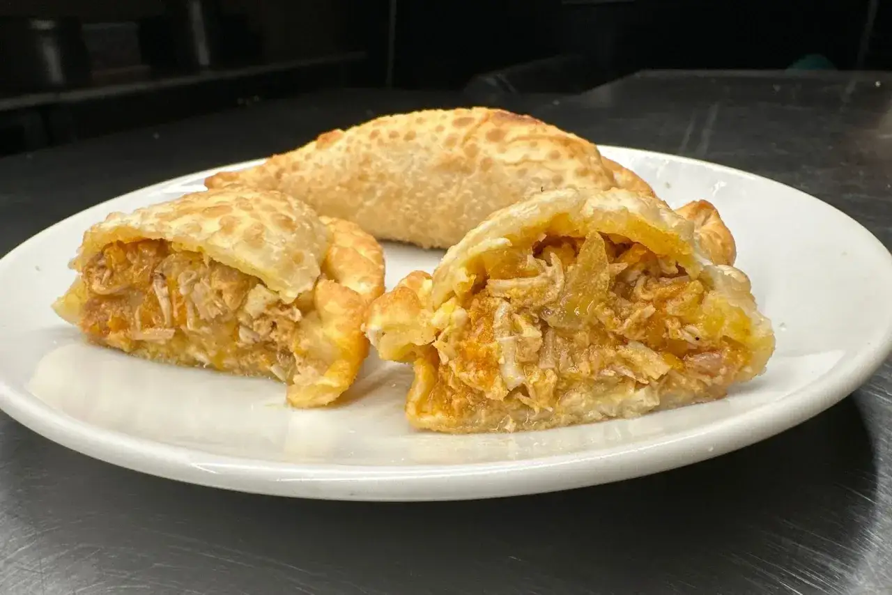 Empanada de pollo jugosa y dorada, lista para disfrutar. Una empanada de pollo cortada revela su relleno sabroso.