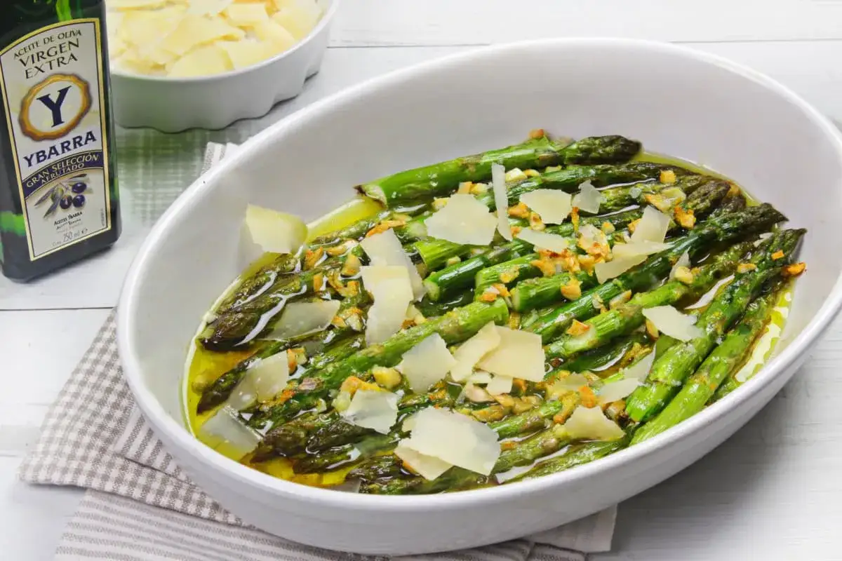 Espárragos verdes tiernos con láminas de queso parmesano y ajo, listos para servir. Ideales para recetas de esparragos verdes.