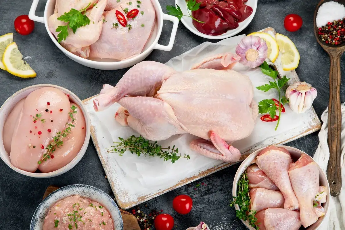 Muslos de pollo, pechugas, un pollo entero y menudillos listos para cocinar. Acompañados de ajo, limón, hierbas y especias.