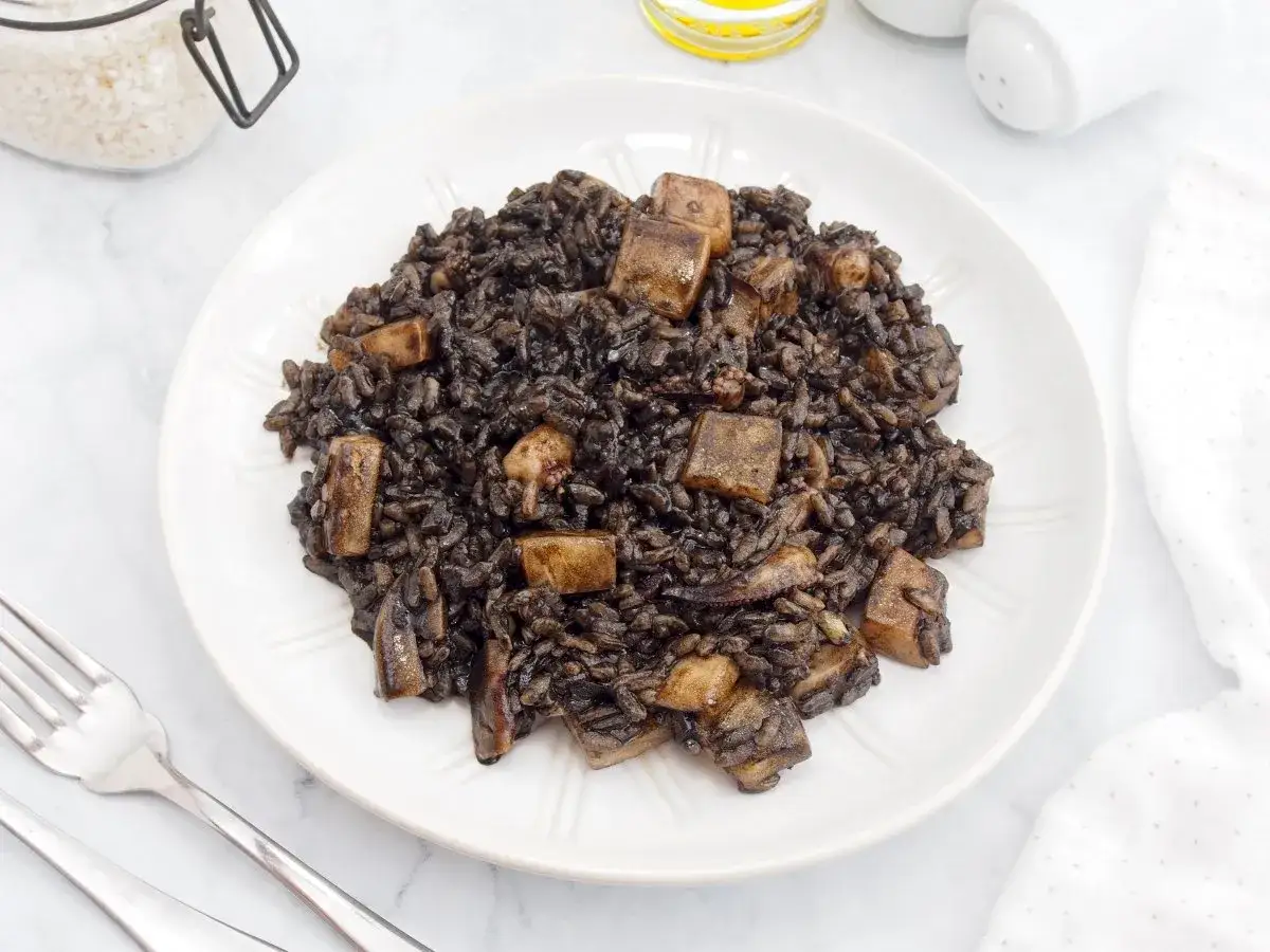 Arroz negro con sepia, un plato oscuro y delicioso, servido en un plato blanco con cubiertos.