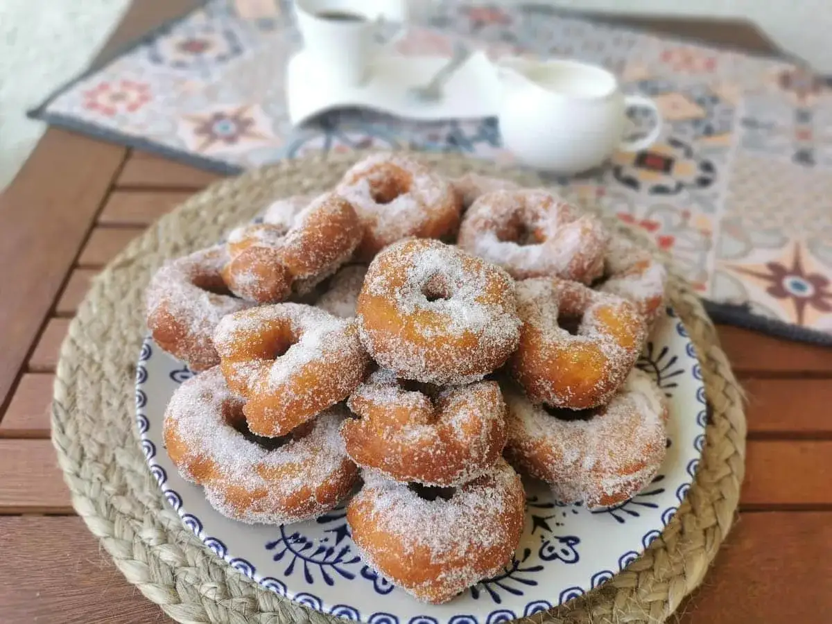 Un plato lleno de rosquillas caseras de toda la vida, espolvoreadas con azúcar. Un placer para la vista y el paladar.
