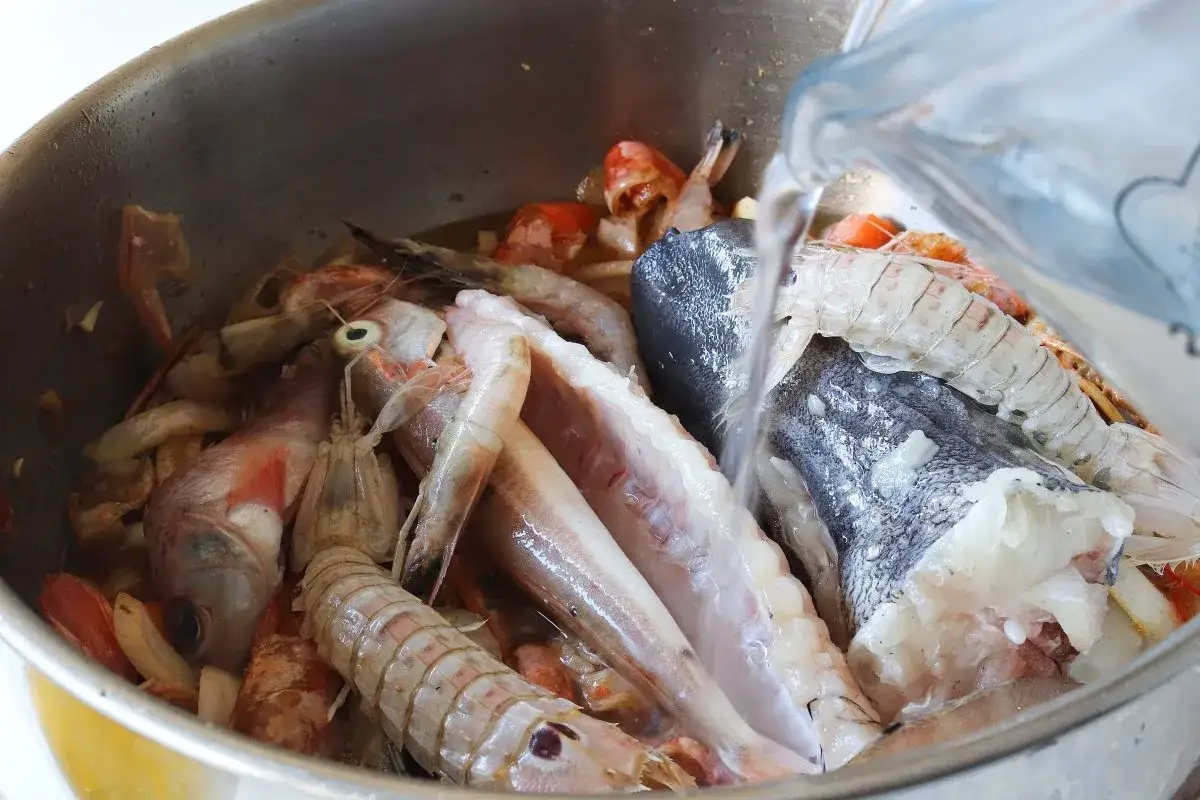 Agua cayendo sobre un bol lleno de gambas, pescado y otros mariscos, prepar&aacute;ndose para un delicioso caldo de pescado.