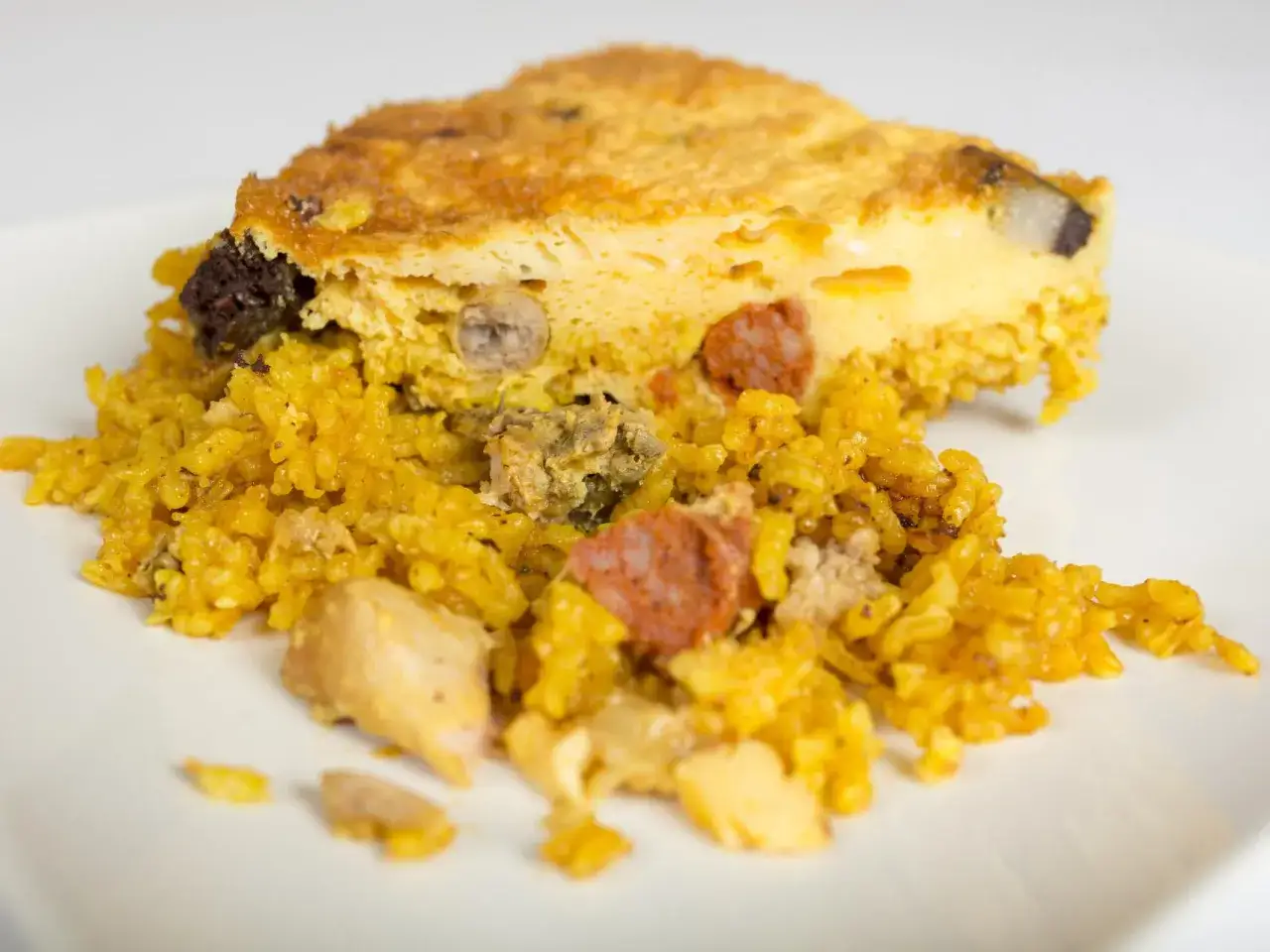 Un trozo de arroz con costra, con trozos de pollo, chorizo y morcilla, servido en un plato blanco.