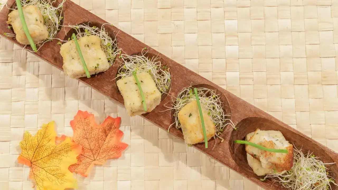 Croquetas caseras con bechamel cremosa, servidas sobre brotes tiernos en una bandeja de madera.
