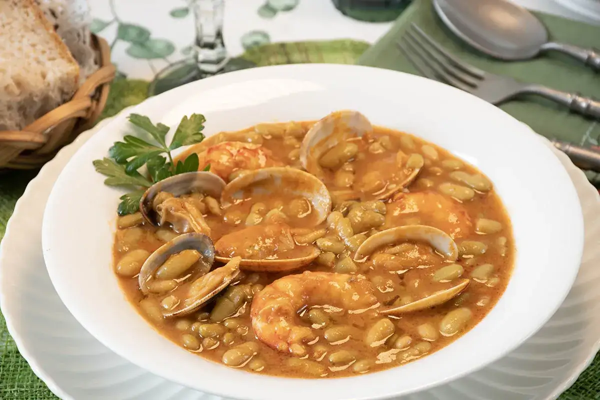 Plato de verdinas con almejas y gambas, servido en un cuenco blanco con perejil. Acompa&ntilde;ado de pan en una cesta.