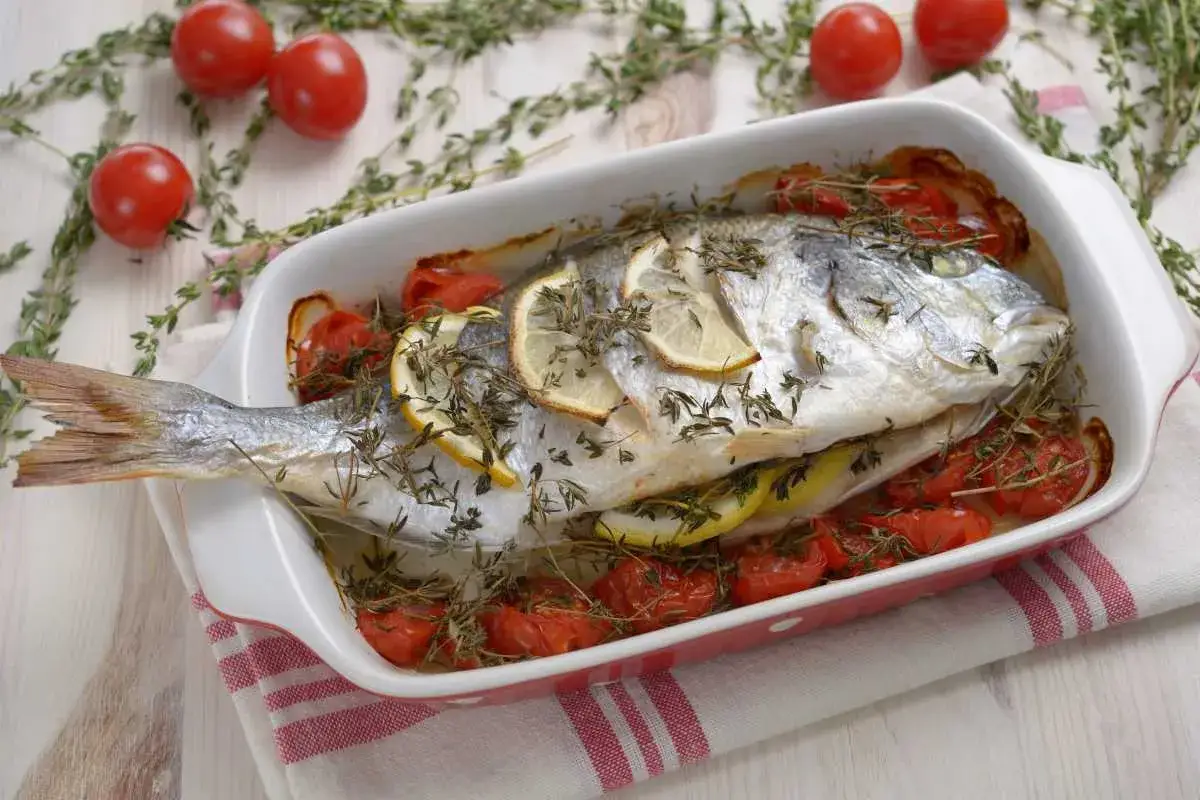 Besugo al horno con rodajas de limón y tomates cherry, listo para servir.