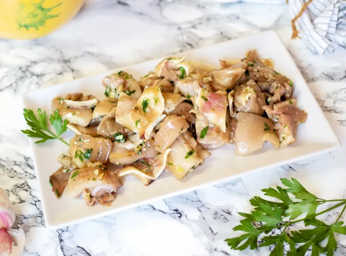 Oreja de cerdo marinada con ajo y perejil, servida en un plato blanco sobre una superficie de mármol.