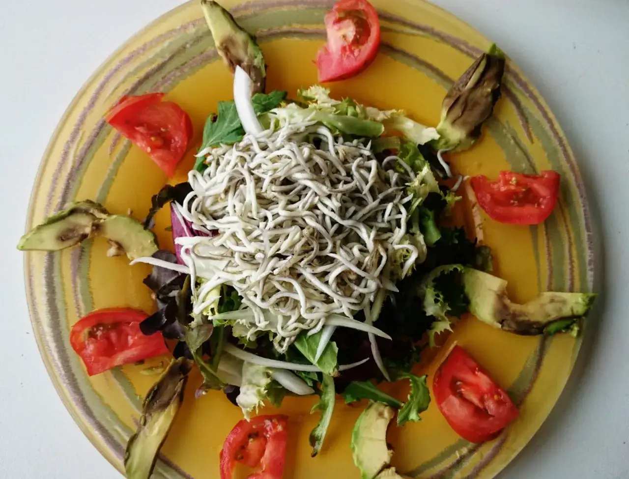 Ensalada de gulas con aguacate y tomate, servida en un plato amarillo con rayas verdes y moradas.