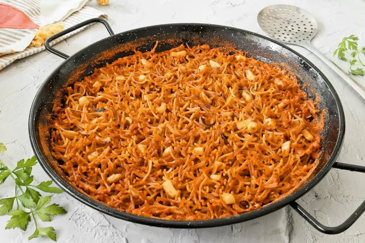 Fideuà con sepia recién hecha en paellera, con fideos finos y trozos de sepia, lista para servir.