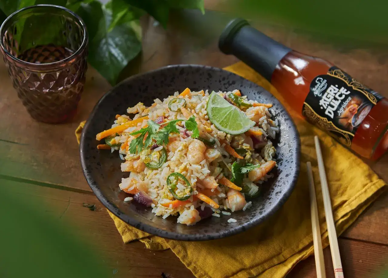 Arroz frito con camarones, zanahoria, jalapeño y cilantro. Una botella de salsa Agri Dulce, que es, está al lado.