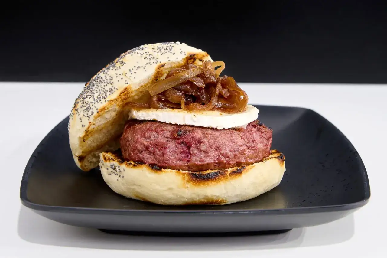 Deliciosa hamburguesa de ternera con queso de cabra y cebolla caramelizada, servida en pan con semillas de amapola.