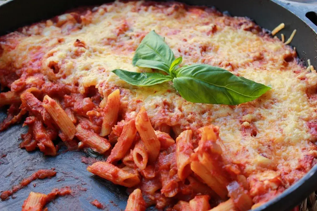 Macarrones al horno con salsa de tomate y queso gratinado, decorados con hojas de albahaca fresca. &iexcl;Un plato casero irresistible!