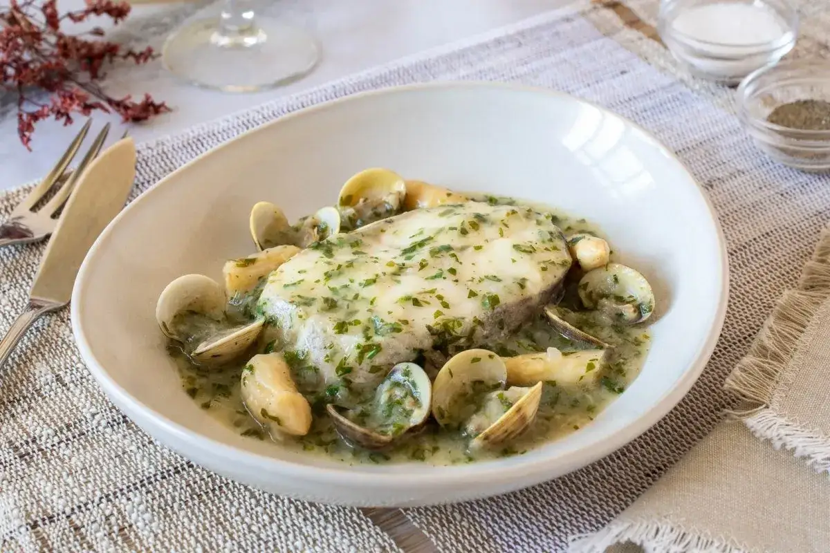 Filete de pescado blanco ba&ntilde;ado en una cremosa salsa verde para pescado, acompa&ntilde;ado de almejas.