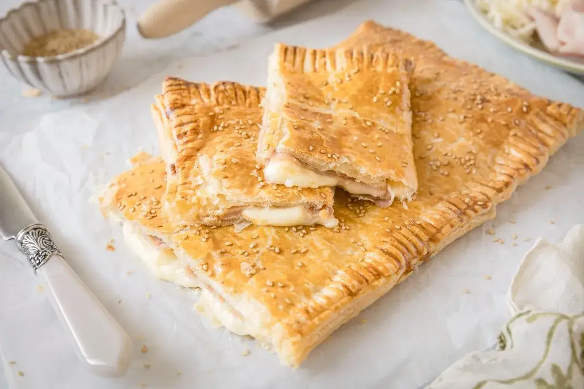 Delicioso hojaldre jamón y queso, dorado y crujiente, con semillas de sésamo. Perfecto para un aperitivo.