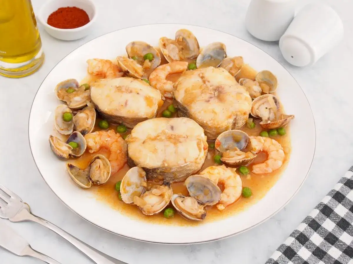 Merluza a la cazuela con gambas, almejas y guisantes en una salsa sabrosa.