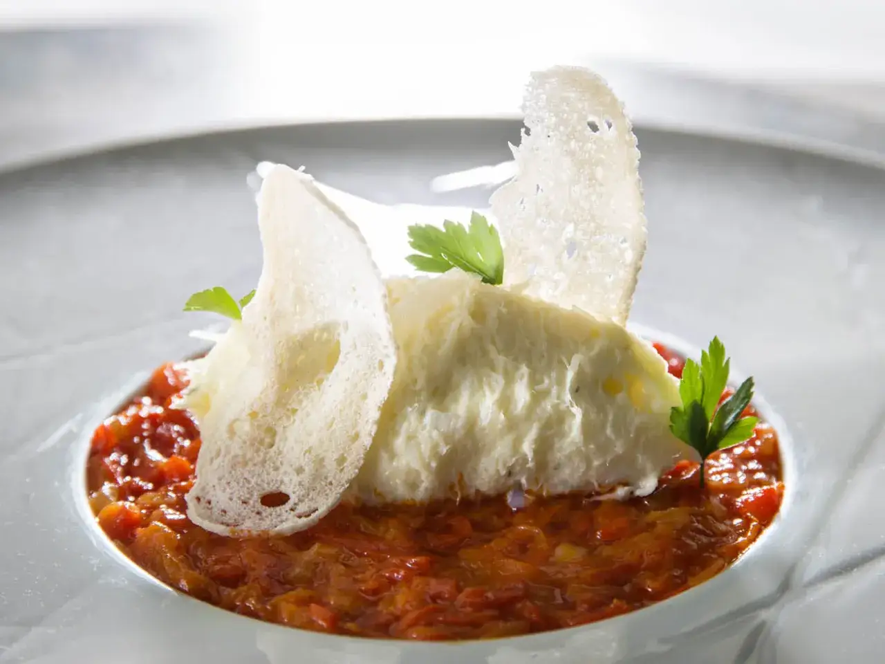 Deliciosa brandada de bacalao cremosa sobre un lecho de pimientos rojos, decorada con crujientes tostadas y perejil fresco.