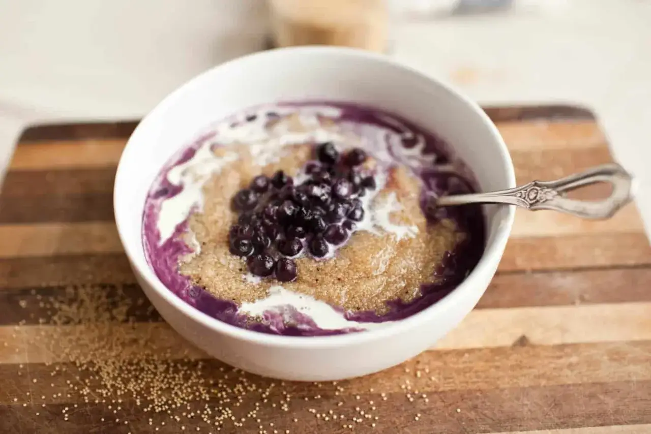 Un tazón de amaranto que es un cereal nutritivo, cubierto con arándanos y crema, servido en una tabla de madera.
