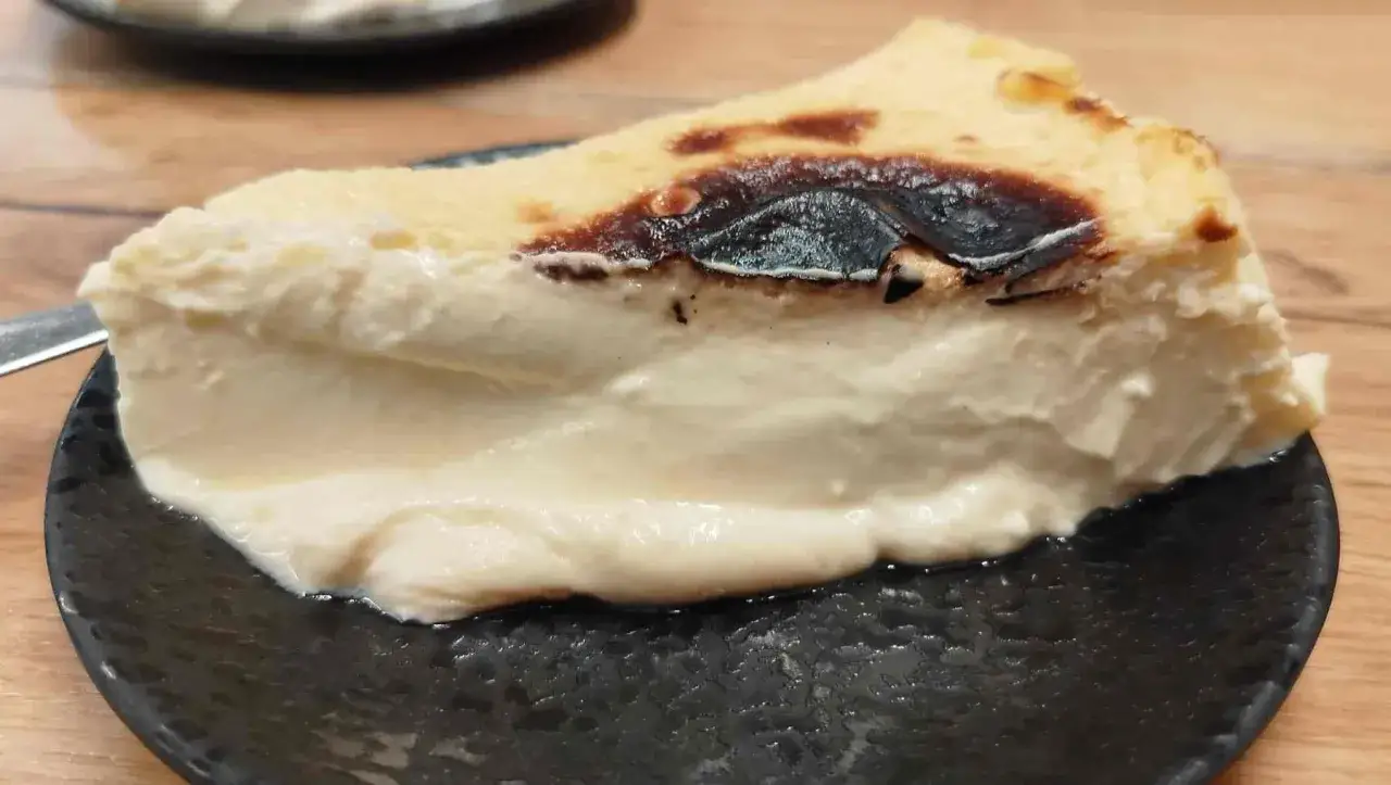 Una porción cremosa de tarta de queso con la parte superior caramelizada, servida en un plato negro.