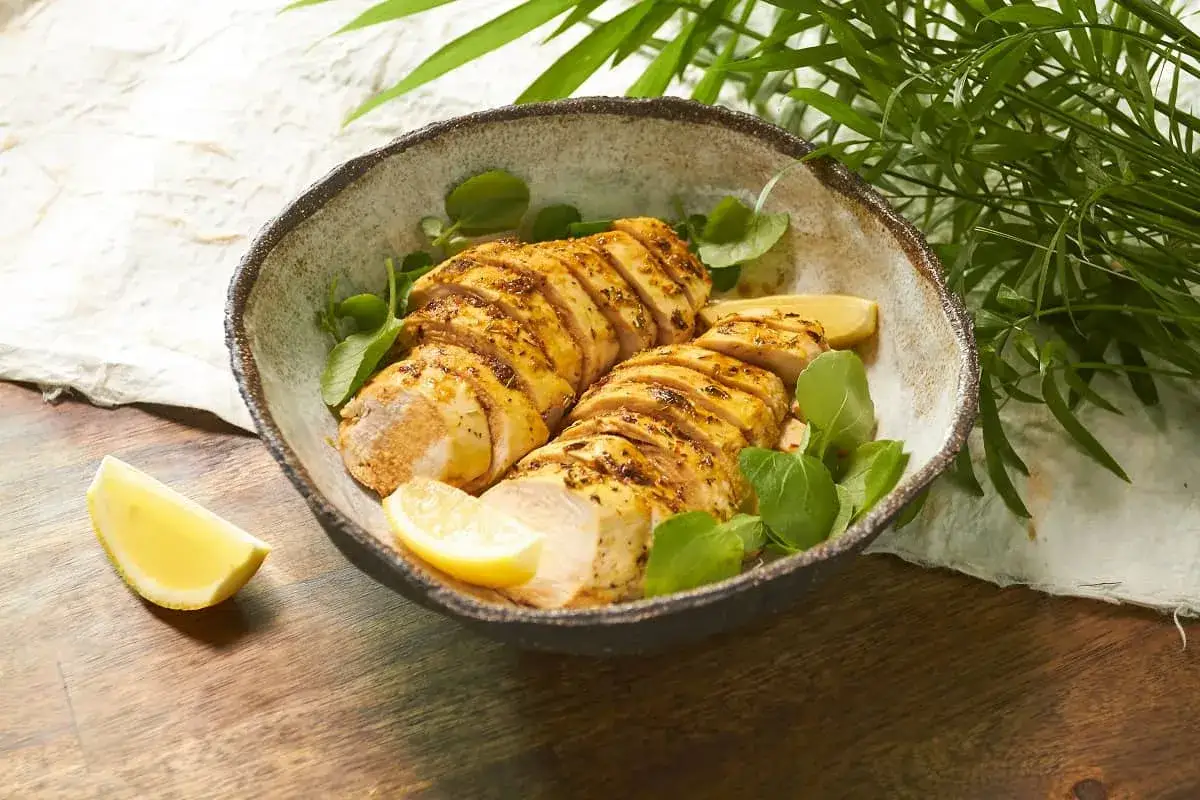Pechuga de pollo al horno, jugosa y dorada, servida en un cuenco rústico con rodajas de limón y hojas verdes.