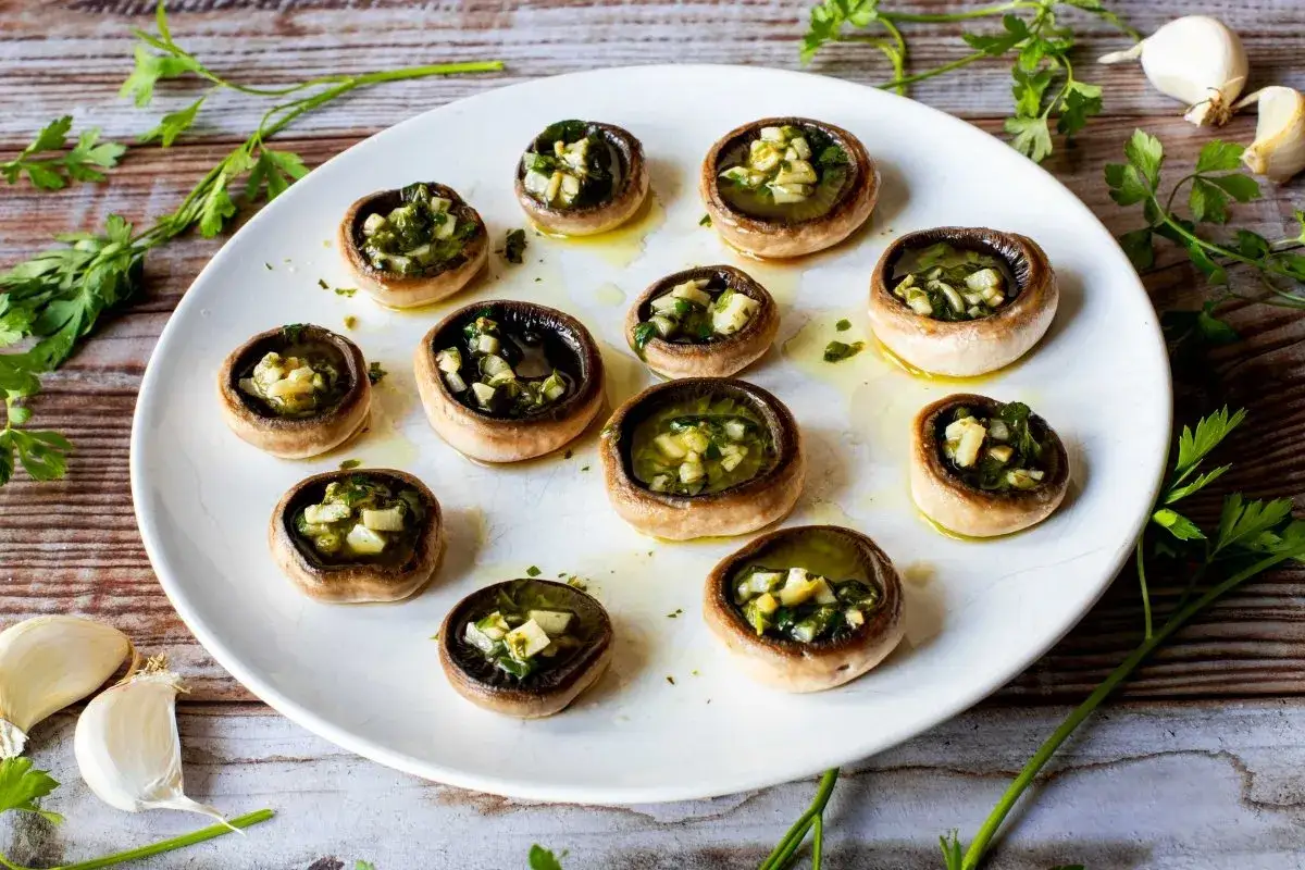 Champi&ntilde;ones a la plancha rellenos de ajo y perejil, servidos en un plato blanco sobre una mesa de madera.