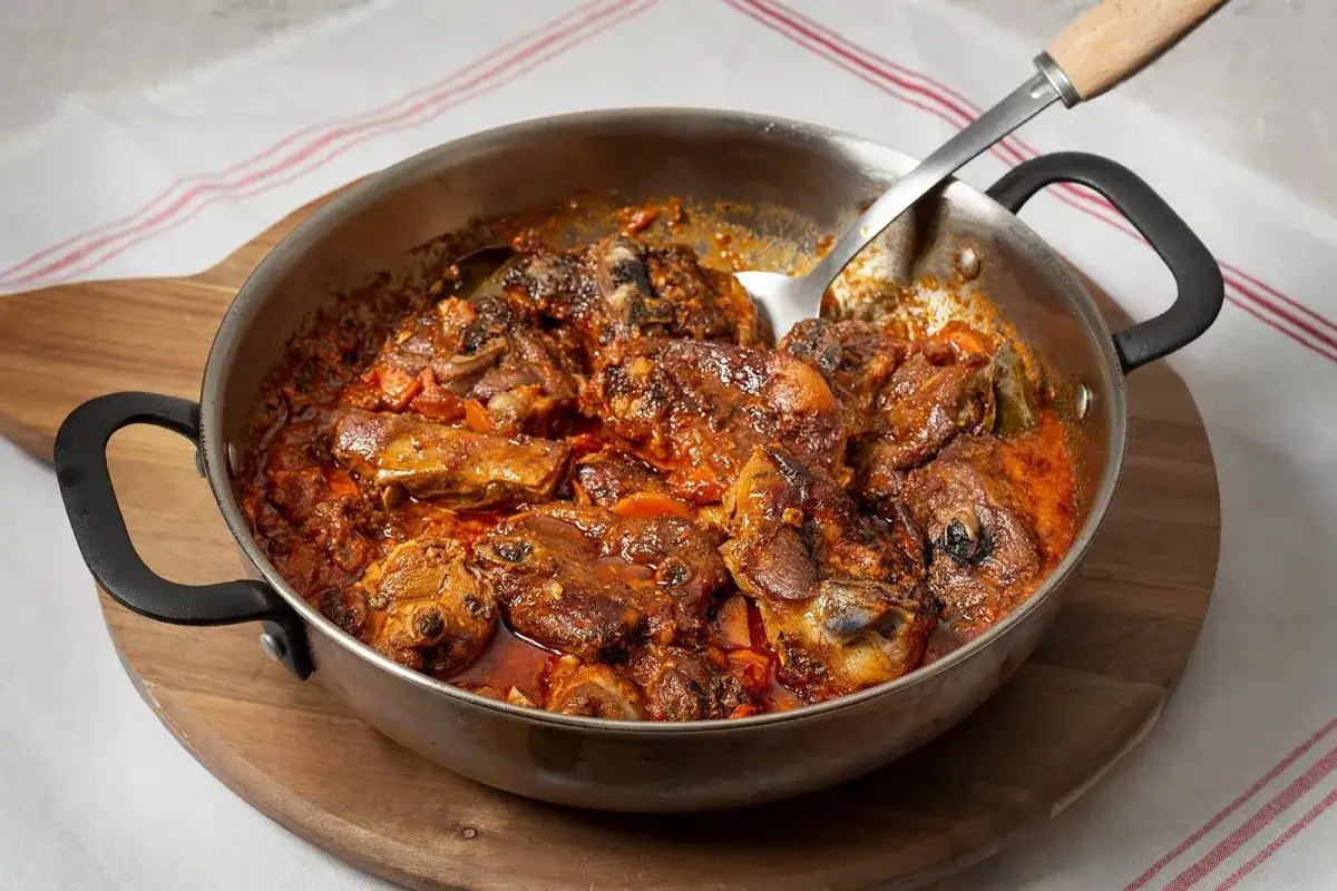 Sabrosa carne de cabra guisada en una sartén, con trozos tiernos y una salsa rica y especiada.