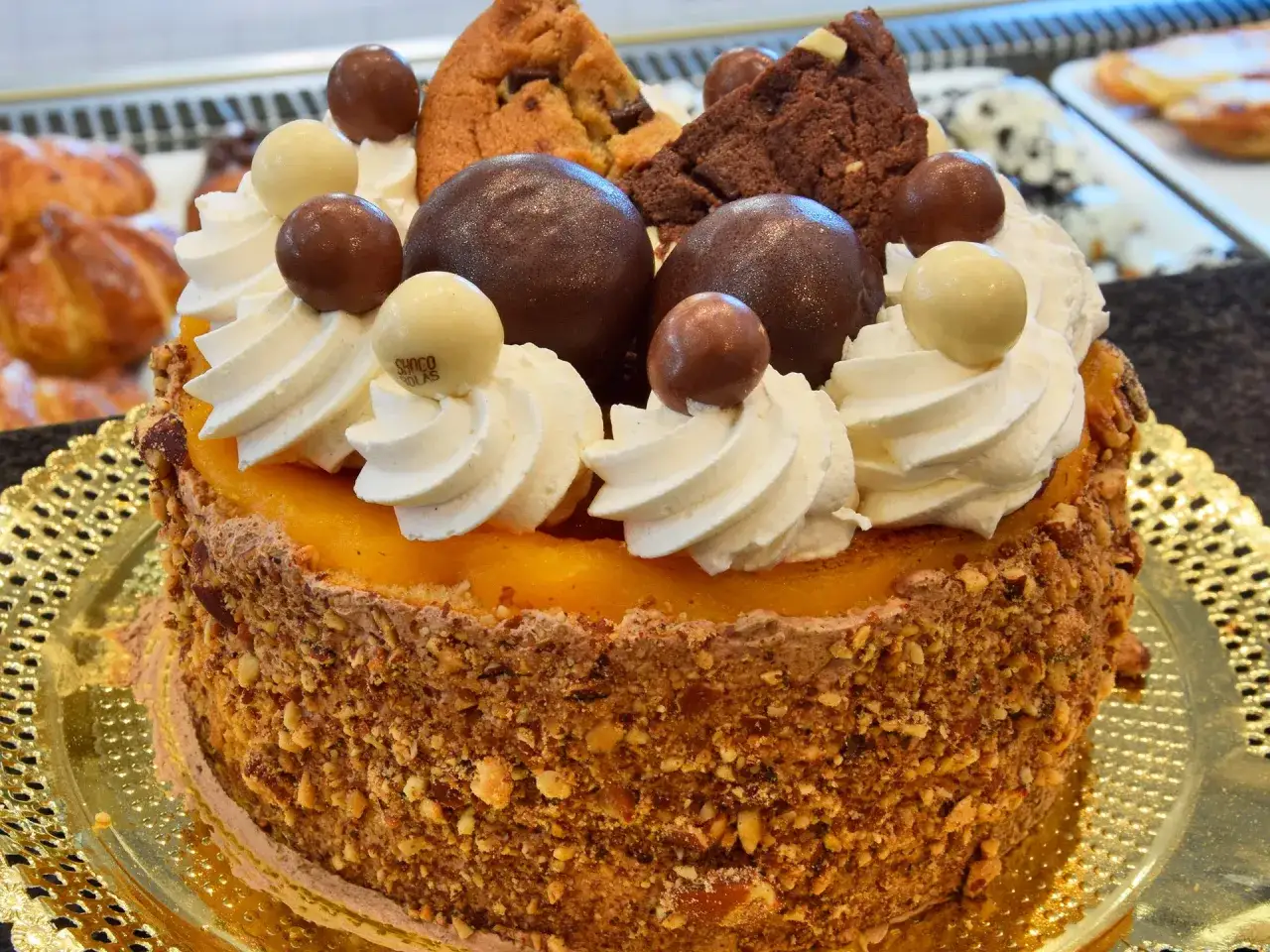 Deliciosa tarta San Marcos, cubierta de nata, chocolate y galletas, con un exterior crujiente de frutos secos.