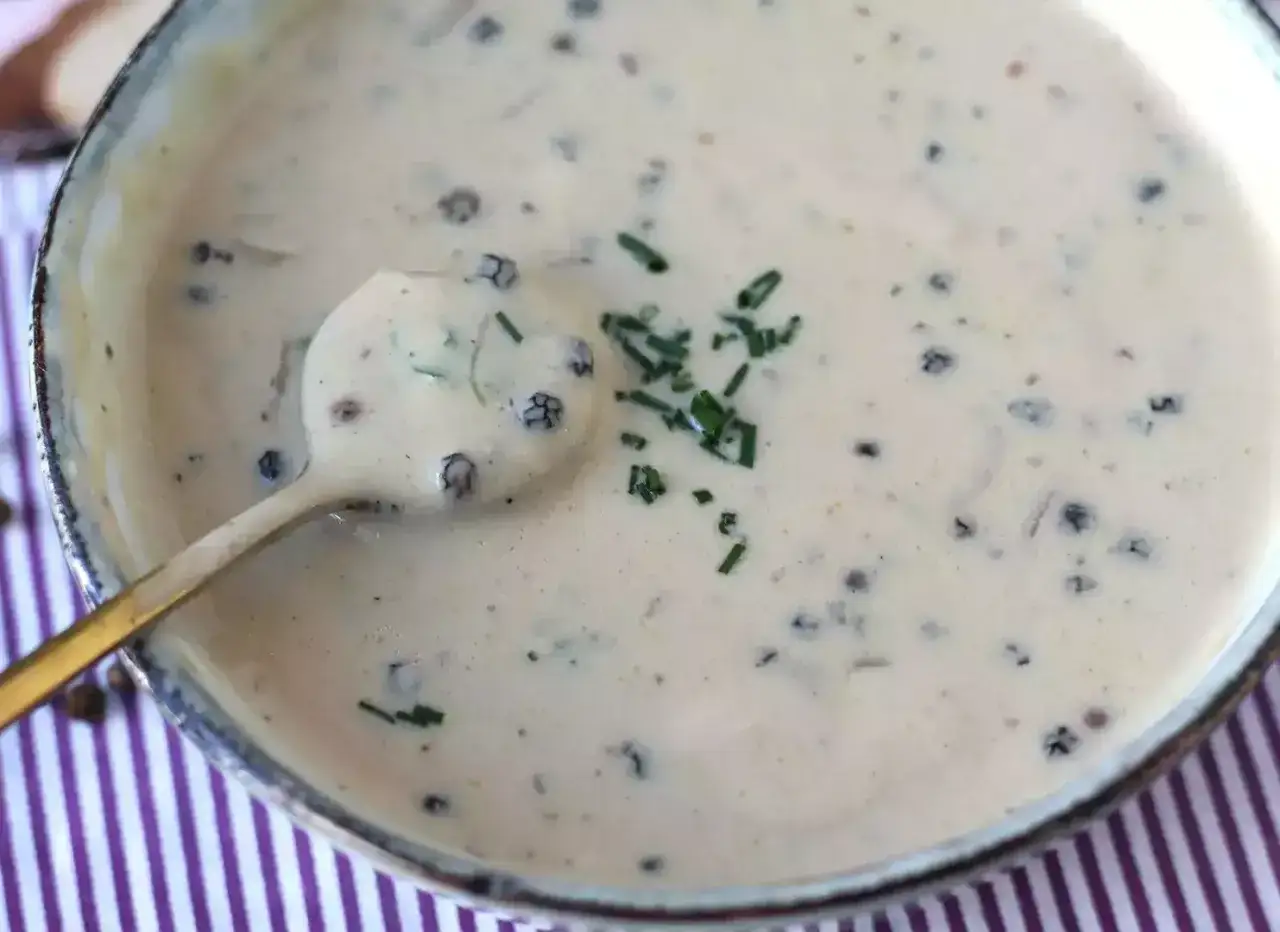 Cremosa salsa a la pimienta, con granos enteros y cebollino fresco, servida en un cuenco sobre un mantel a rayas.