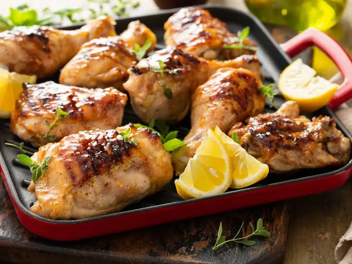 Jugosos contramuslos de pollo a la parrilla, dorados y con hierbas frescas, acompañados de gajos de limón.