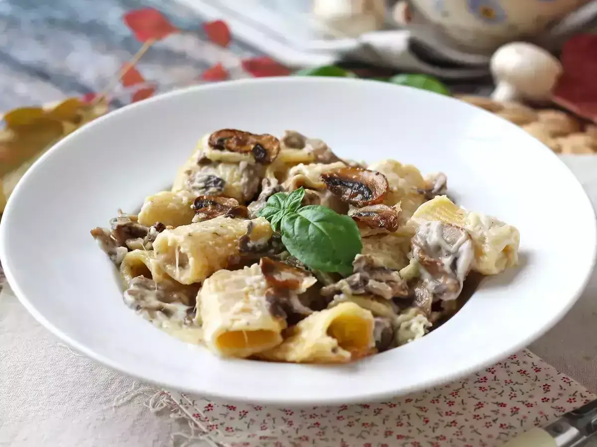 Deliciosa pasta con champiñones cremosos y un toque de albahaca fresca, servida en un plato blanco.